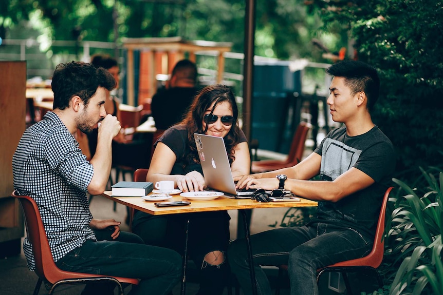 Two men and a woman having a meeting in an outdoor cafe setting for a story about creating a mentally healthy workplace.