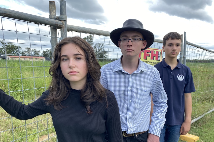 Three students stand in front of a fence watching the empty field where there school is supposed to be. 