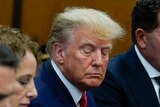 Donald Trump glances down, his face in a tight frown, sitting between two men in suits