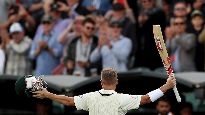 Seen from behind, Australia batsman David Warner raises his bat and helmet to the crowd.