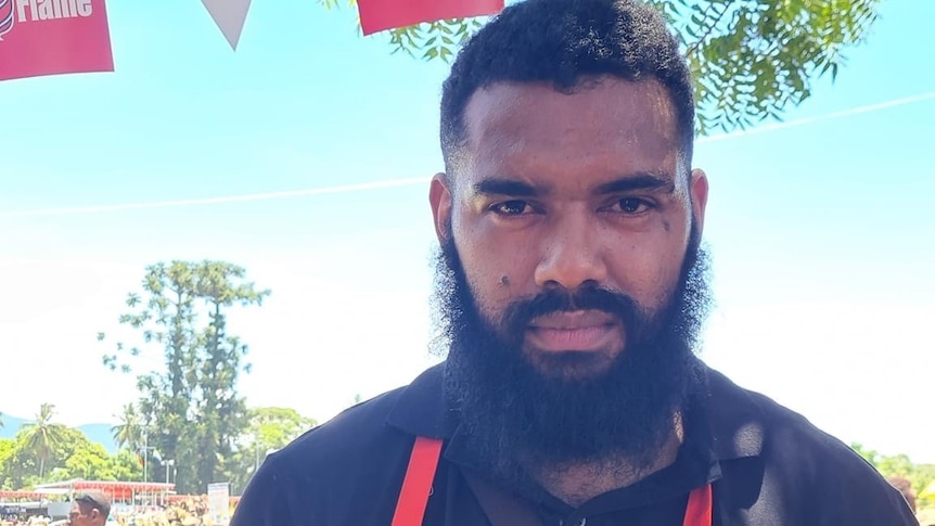 Man in red apron holds out plate of chicken.