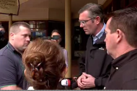 Three men and a woman stand in a circle speaking to each other, surrounded by news cameras.