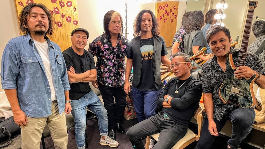 Six Nepalese men in a dressing room with various instruments.