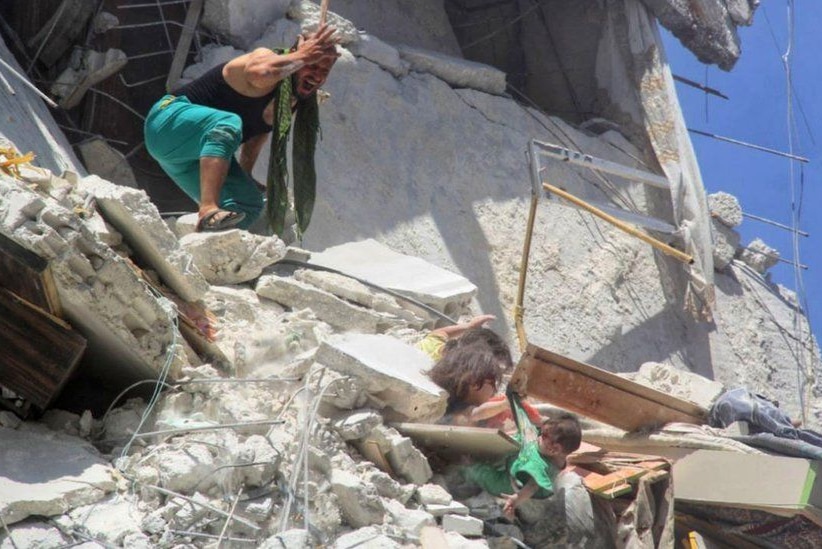 A man screams as he looks down at two little girls hanging from rubble from the side of a destroyed building.