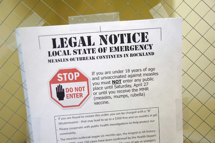 A Rockland County Health A4 poster warning of a local measles outbreak taped against a yellow tiled wall.