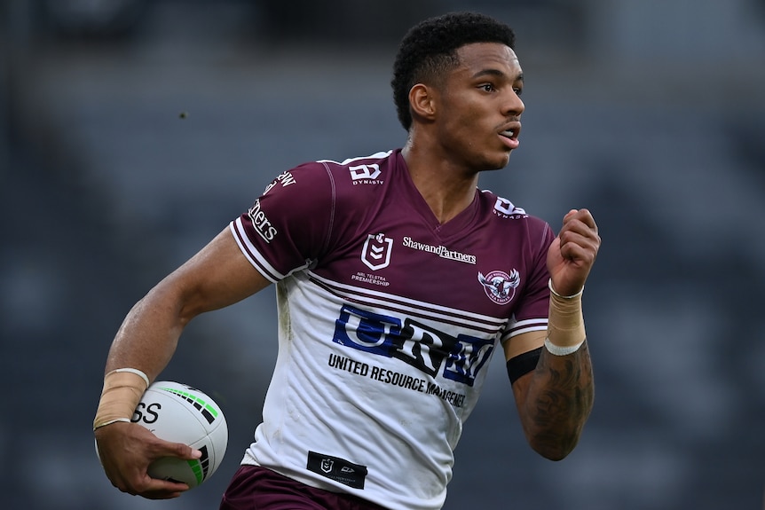 A Manly Sea Eagles NRL player runs with the ball in his right hand.