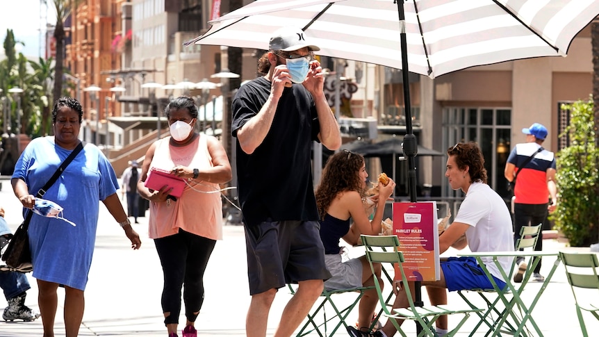 Two out of five pedestrians along a sunny street are wearing face masks 