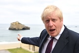 UK Prime Minister Boris Johnson, wearing a black suit, points out to the Atlantic Ocean.