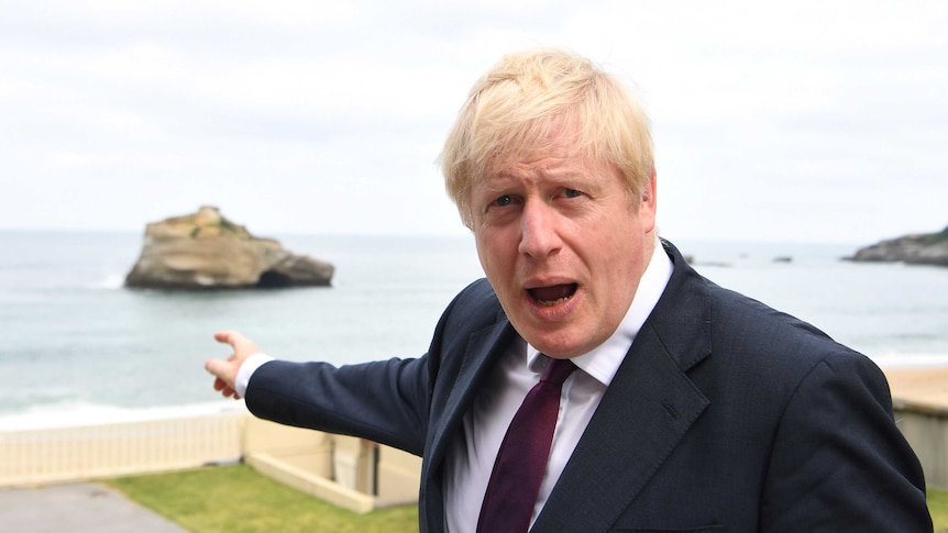 UK Prime Minister Boris Johnson, wearing a black suit, points out to the Atlantic Ocean.