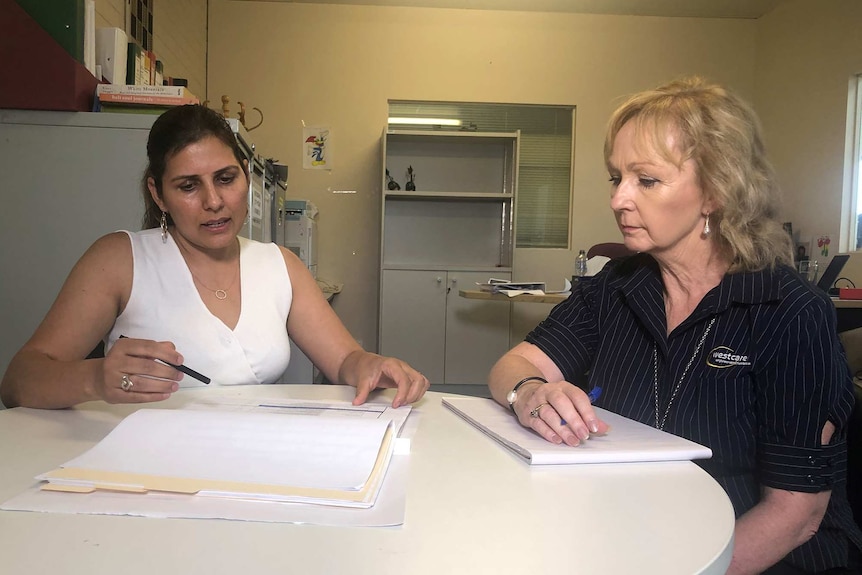 Two women sit at a table looking at papers.