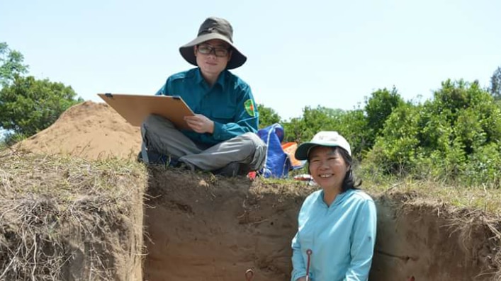 Two Vietnamese archaeologists sit at dig site.