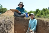 Two Vietnamese archaeologists sit at dig site.