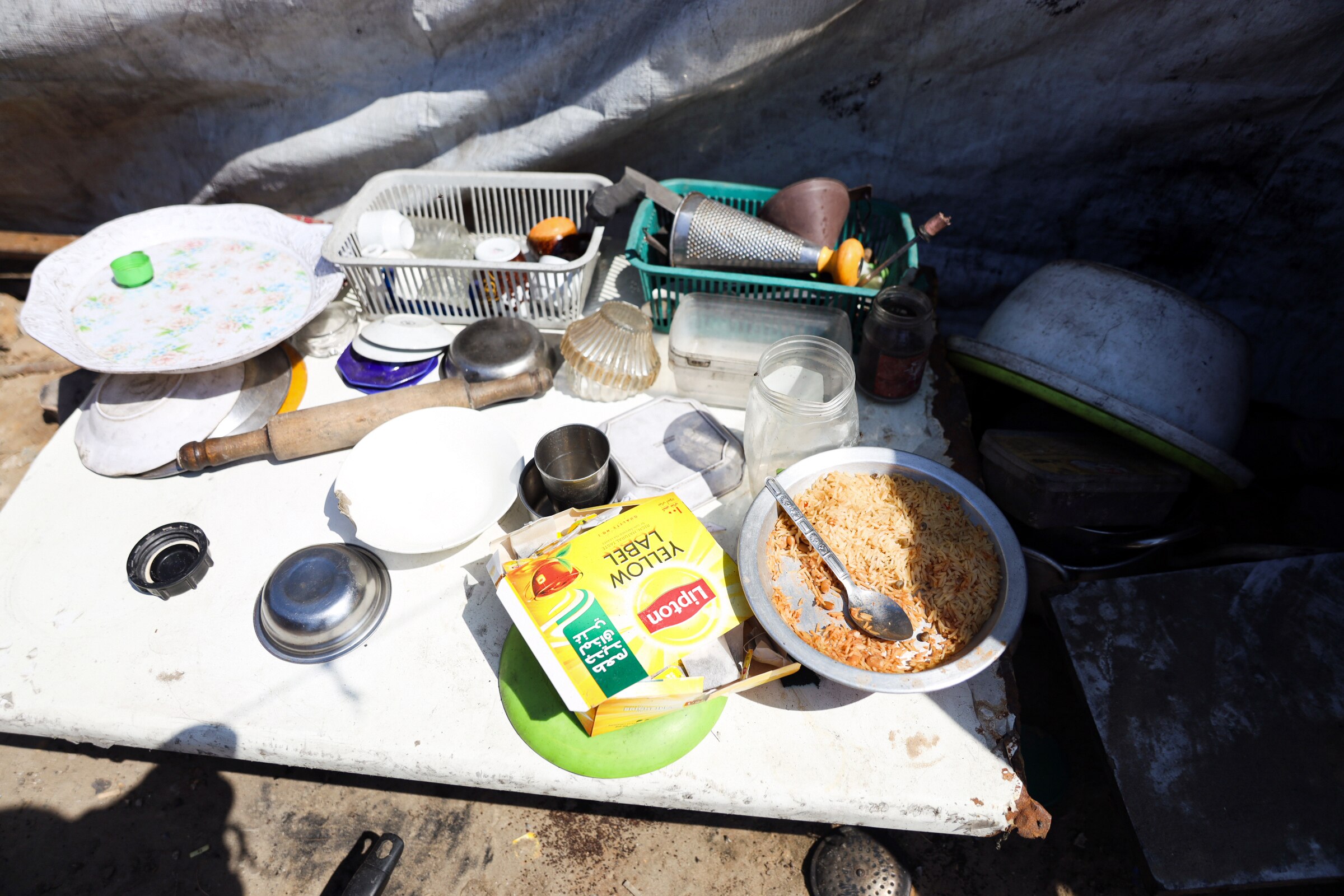 A bowl of rice and several utensils are laid out on a plank on the ground