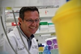 A man in a white lab coast with glasses sits down and looks at test samples in a laboratory