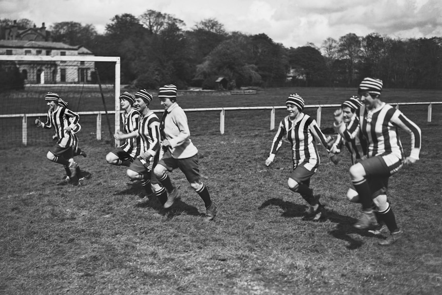 A black and white image of women running on a soccer field warming up.