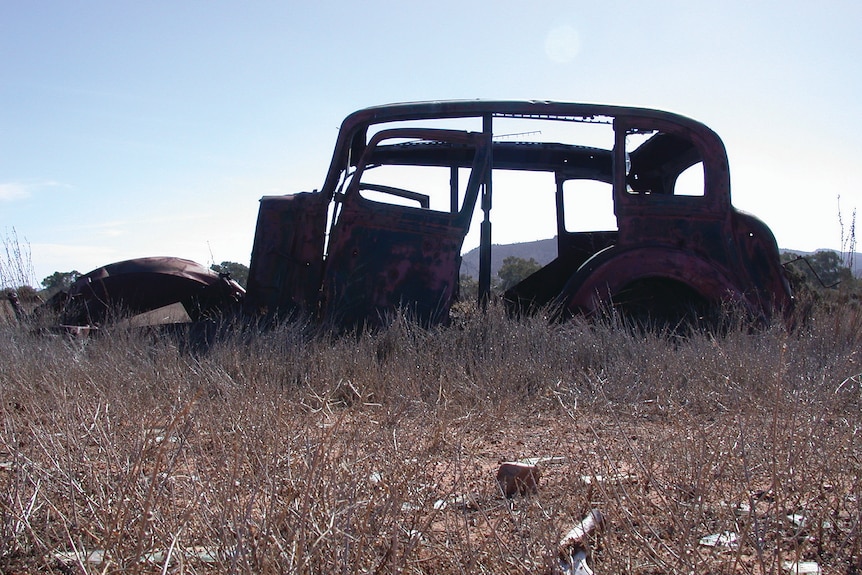 A rusting pile of metal on dry grass with the sky in the background.