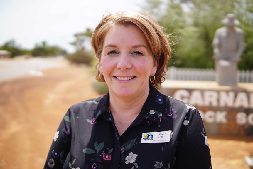 Karen Oborn looks into the camera. She is smiling, her hair is short and she is wearing gold earrings and a black floral shirt.