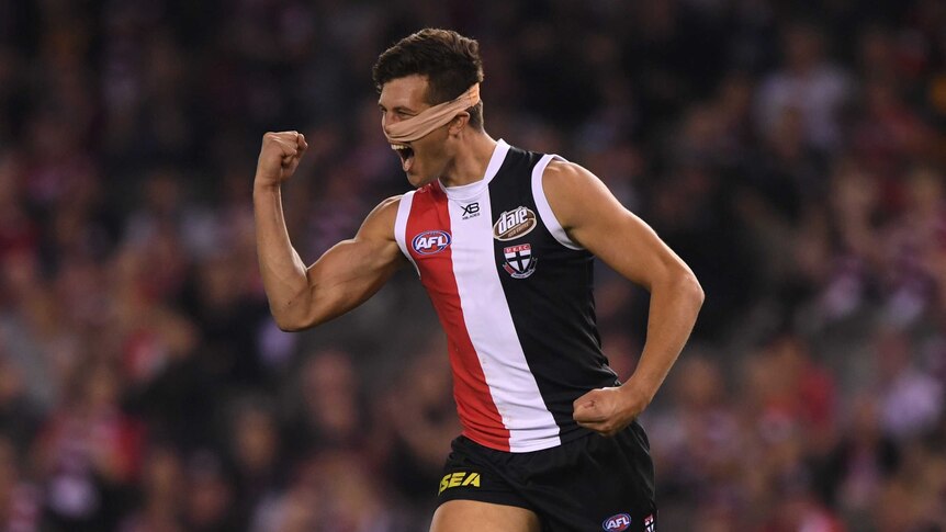 An AFL player with a bandage around his face pumps his fist in celebration after kicking a goal