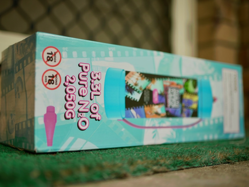 An image of a light blue cardboard box containing nitrous oxide on a welcome mat at a front door with flyscreen in background