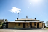 Exterior photo of a one-storey building with sloping corrugated iron roof and broad verandah