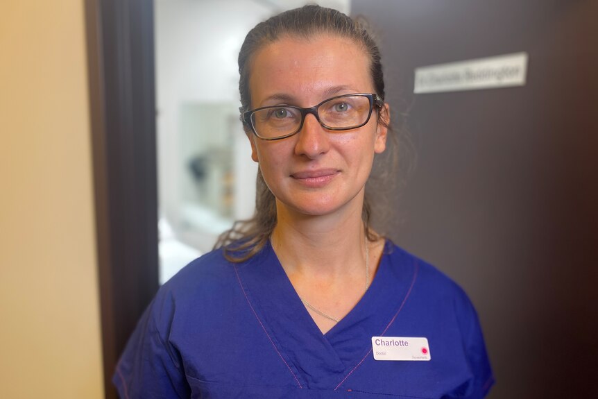 A woman with glasses wearing blue scrubs with a nametag that says Charlotte.