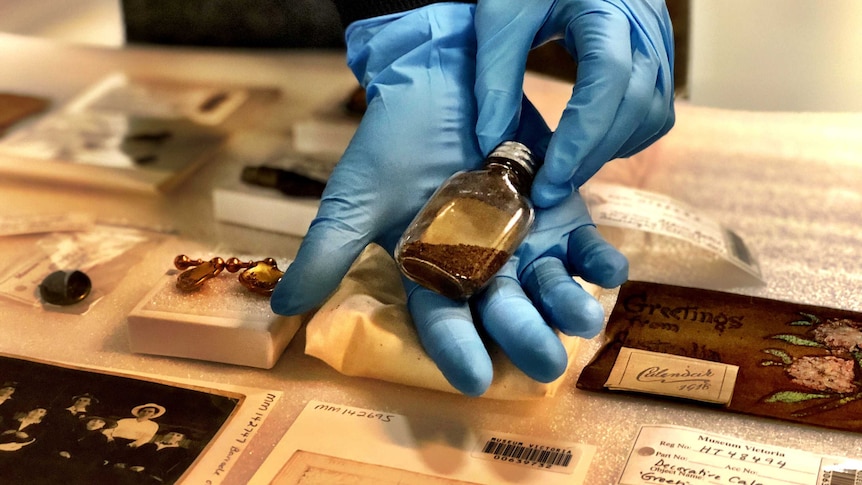 A person holds a small bottle of soil in gloved hands.