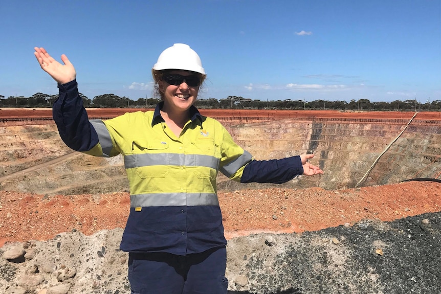 writer dressed in hi-vis posing in front of an open pit mine. 