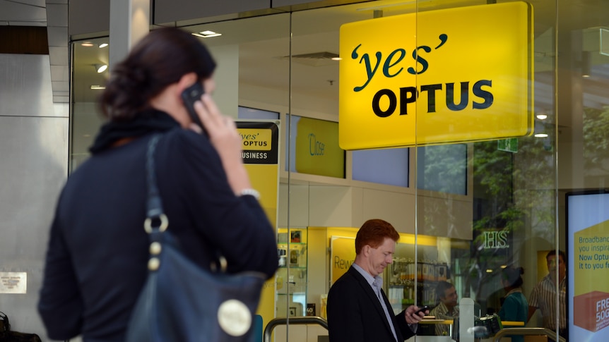 A woman uses her phone outside an Optus store as a man looks at his.
