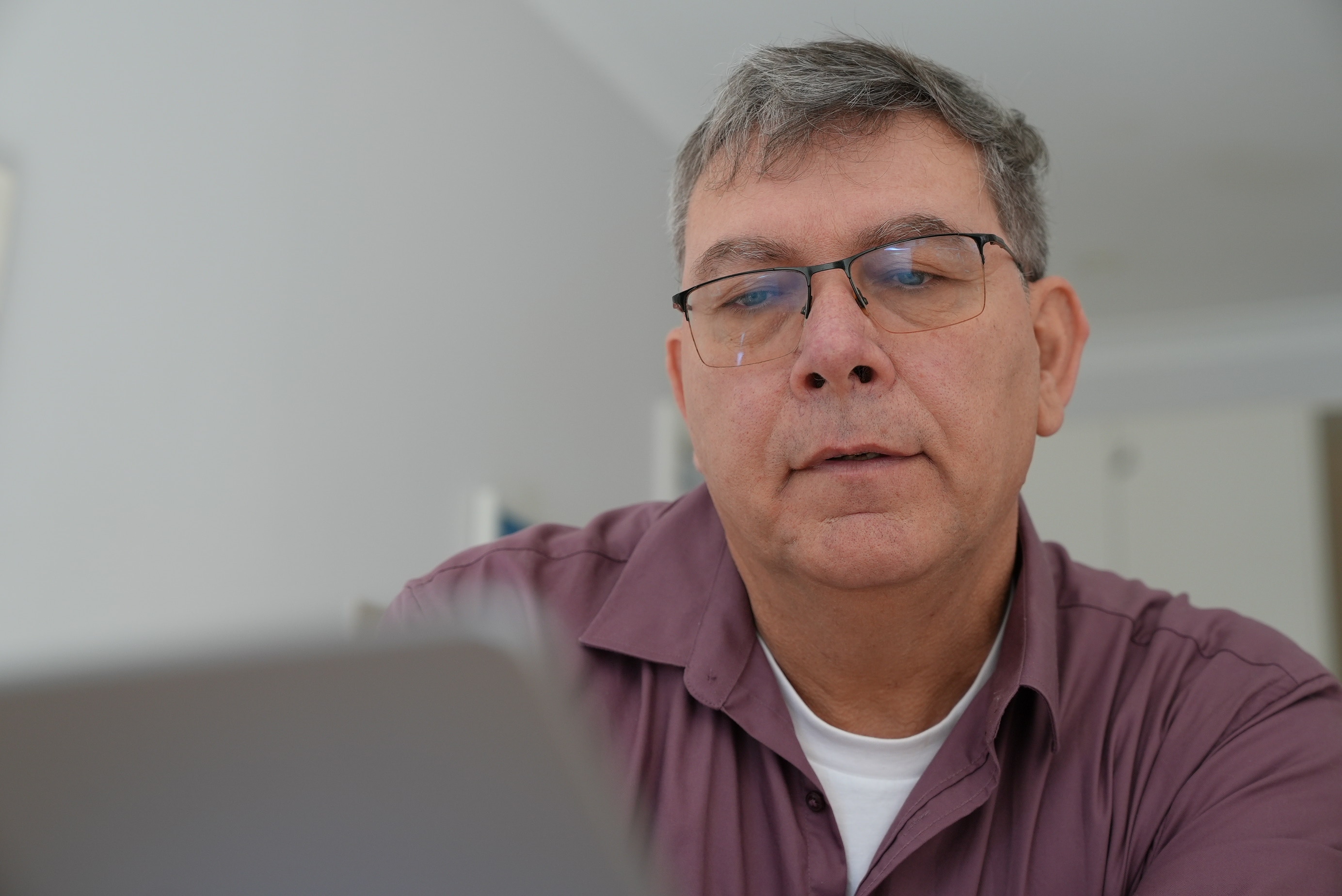 A man looking at his lapop and is wearing a purple button up shirt and glasses