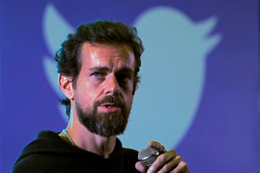 Close-up of Twitter CEO Jack Dorsey speaking into a mic with the Twitter bird logo in the background