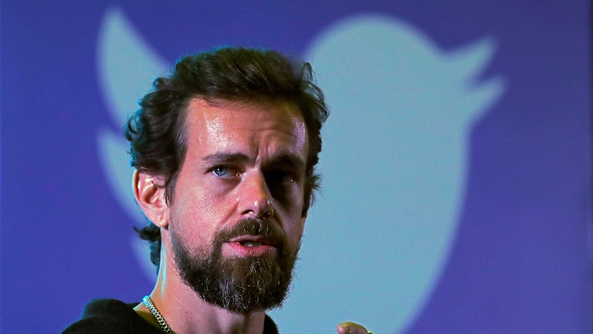 Close-up of Twitter CEO Jack Dorsey speaking into a mic with the Twitter bird logo in the background