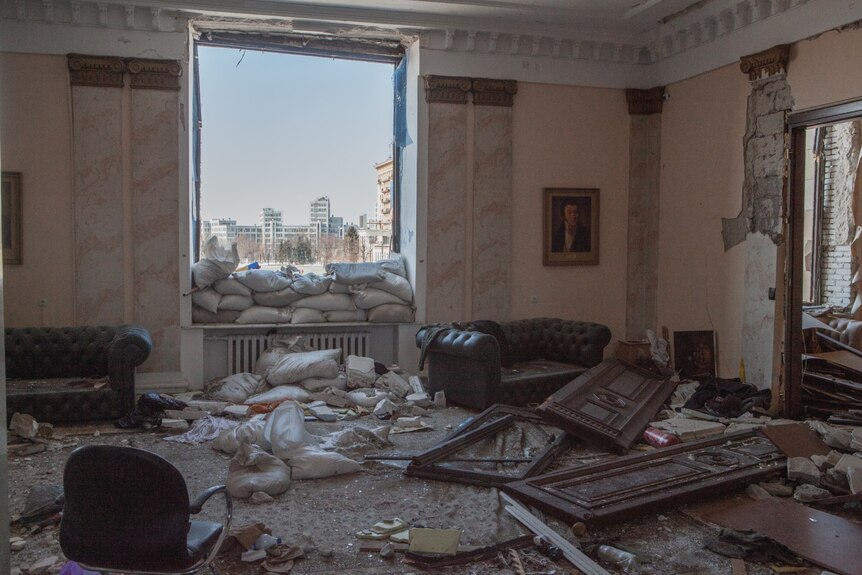 A room with sand bags against a window is falling apart following a bombing on the building. 