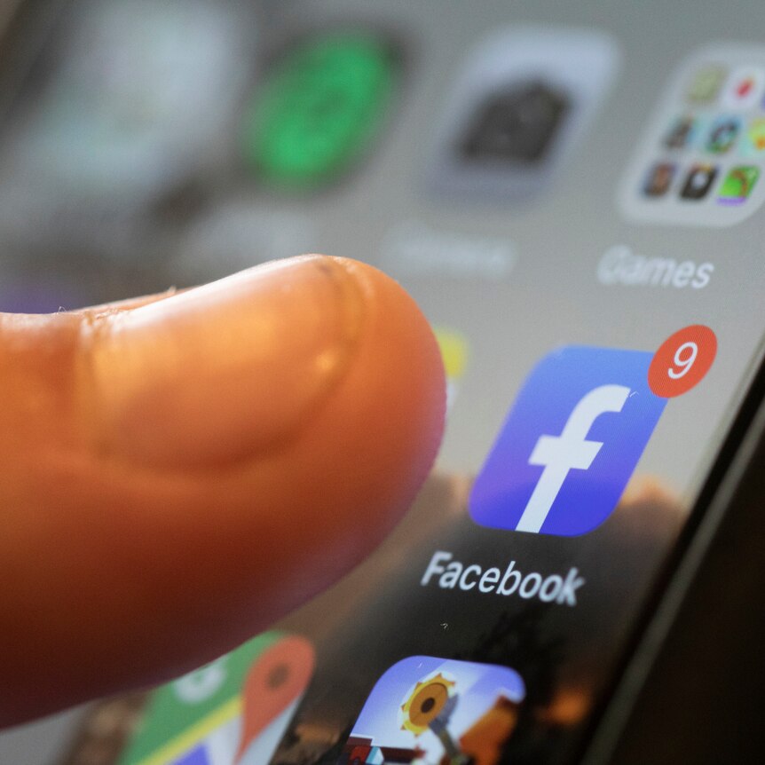 A person's thumb edges towards a Facebook app icon on a smartphone. 