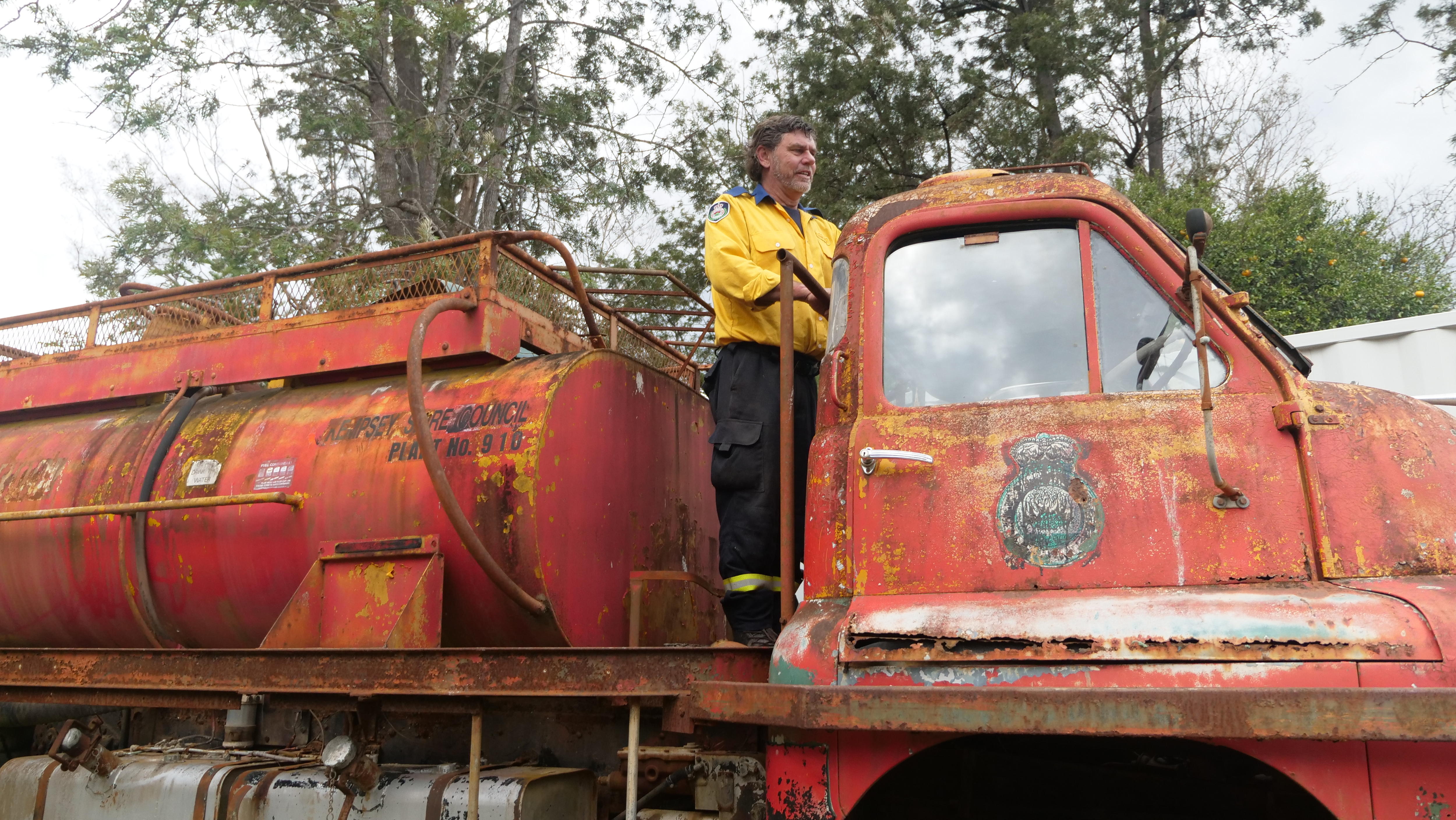 A firefighter stands on the back of an old fire truck.