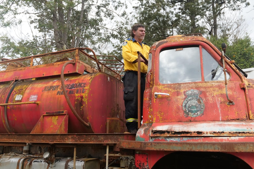 A firefighter stands on the back of an old fire truck.