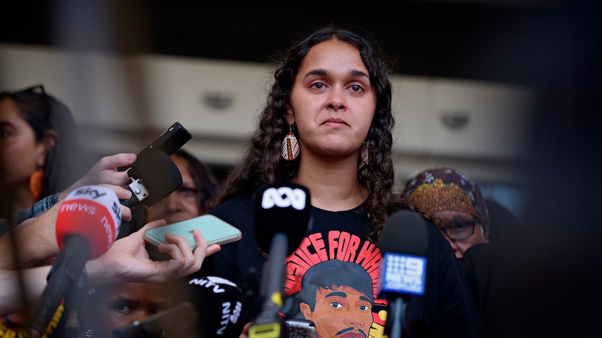 A First Nations woman speaks while journalists hold microphones, with the NT Supreme Court in the background.