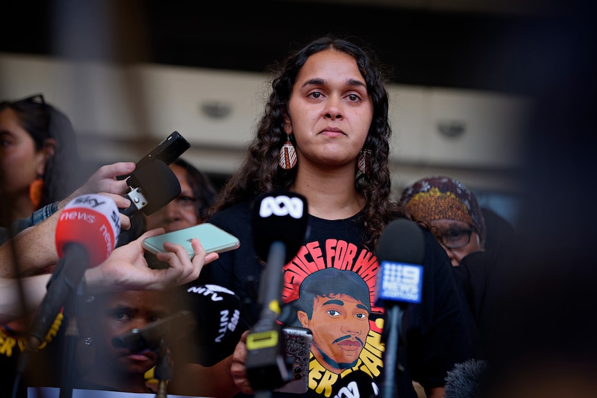 A First Nations woman speaks while journalists hold microphones, with the NT Supreme Court in the background.