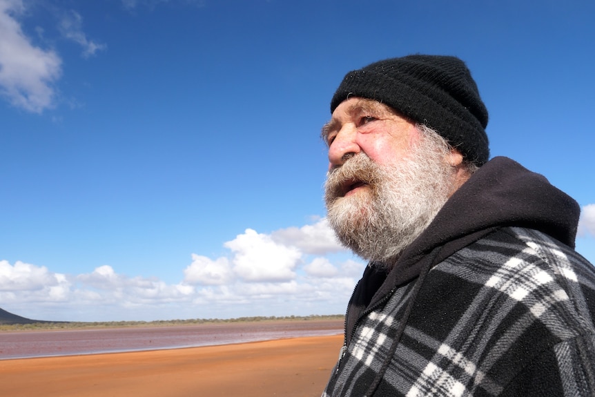 An Aboriginal man looking out over vast blue skies, water and red dirt.