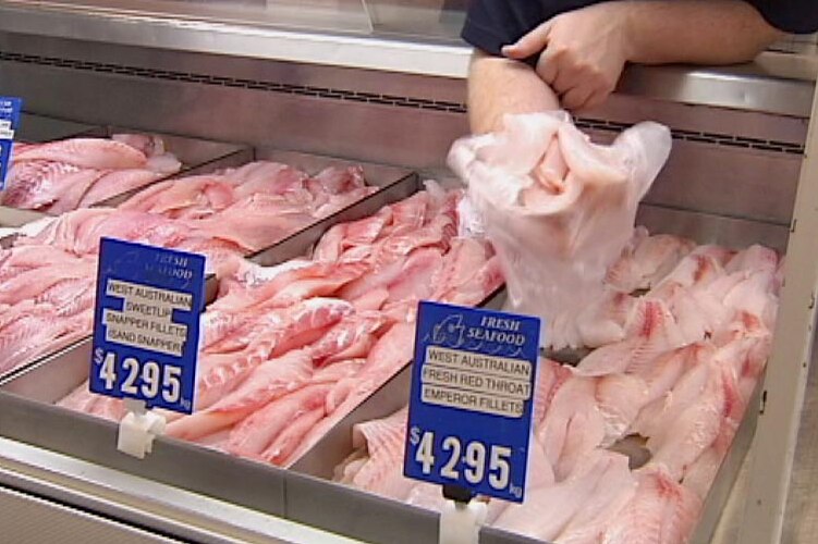 Fishmonger reaches into cabinet of fish fillets