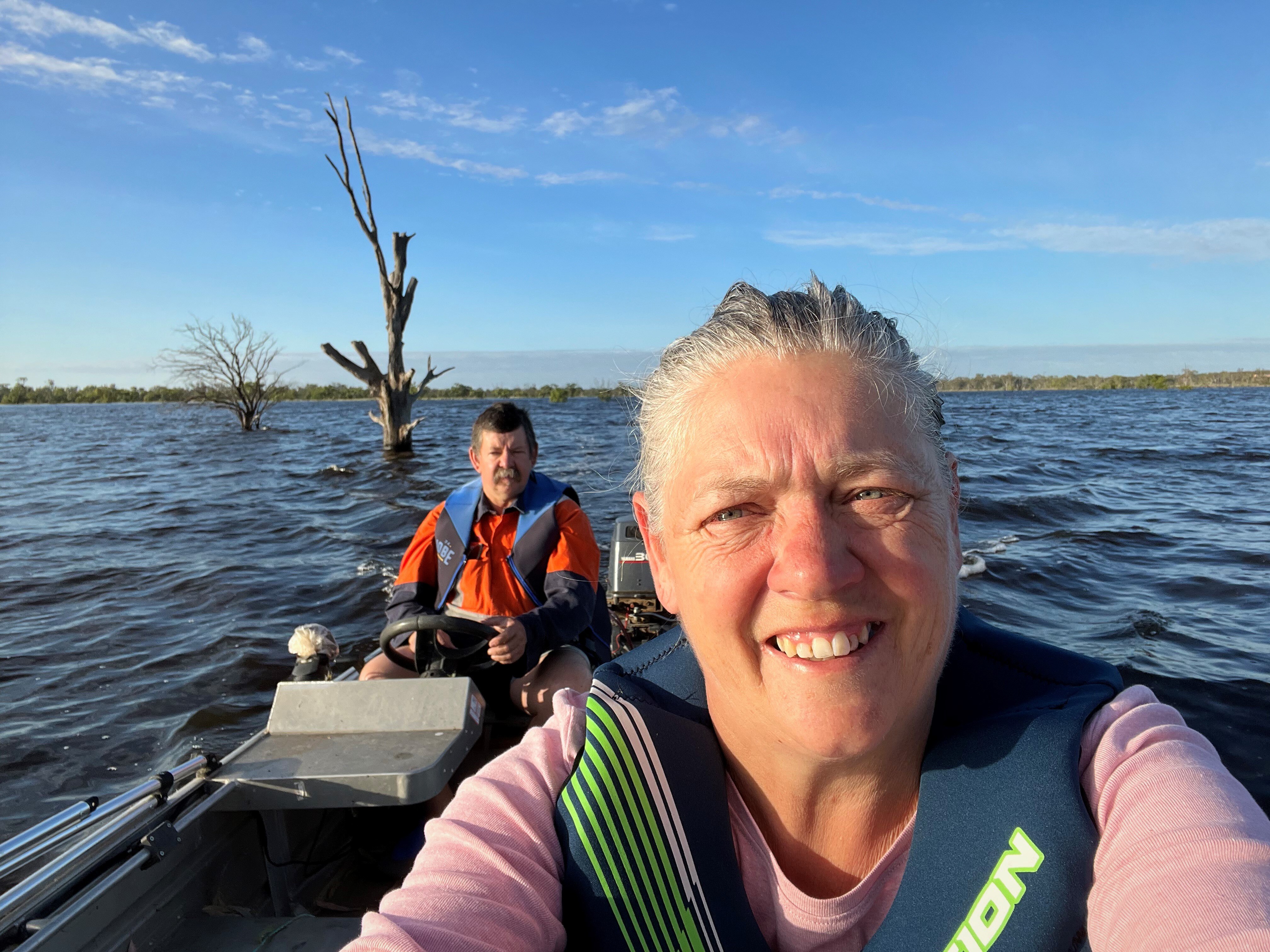 a woman and man on a boat, with choppy blue waves below, and bright blue sky above. They are wearing lifejackets and look happy.