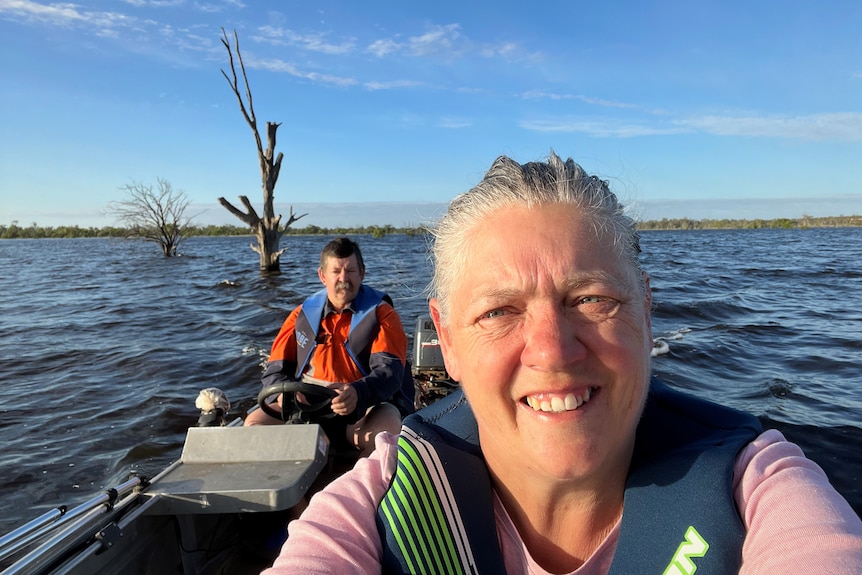 a woman and man on a boat, with choppy blue waves below, and bright blue sky above. They are wearing lifejackets and look happy.