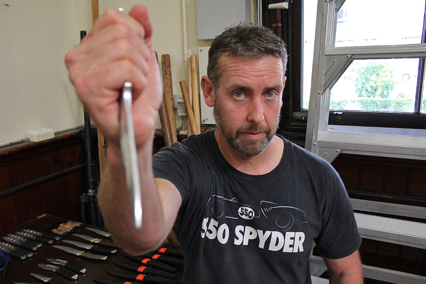 Fight director Andy Fraser holds a fake dagger aimed at the camera.