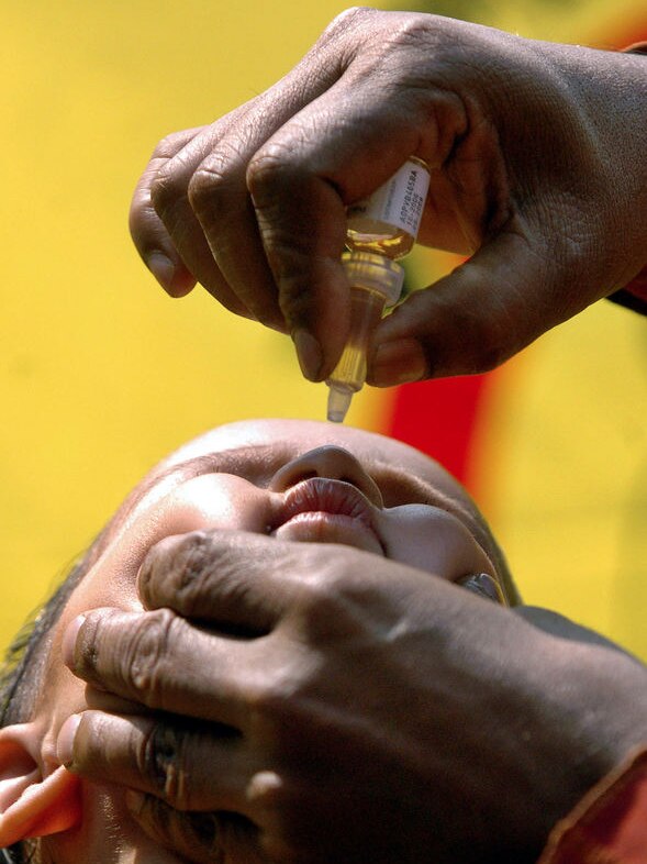 A health worker administers polio drops to a boy.