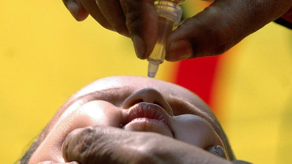 A health worker administers polio drops to a boy.