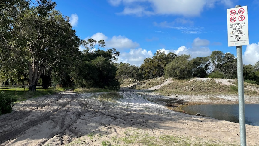 Sand with tyre marks, dam and sign saying no vehicles