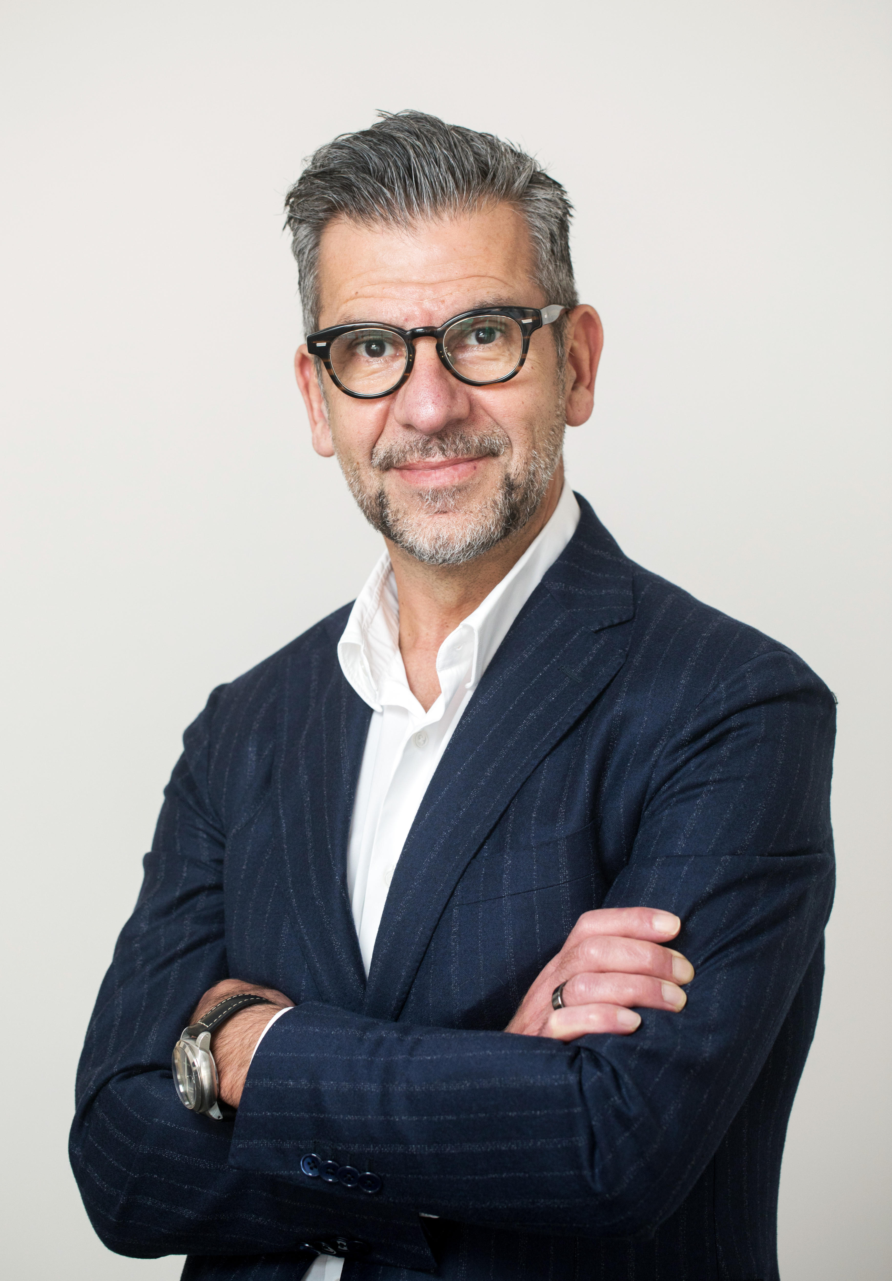 Un hombre de mediana edad con traje azul oscuro y gafas. 