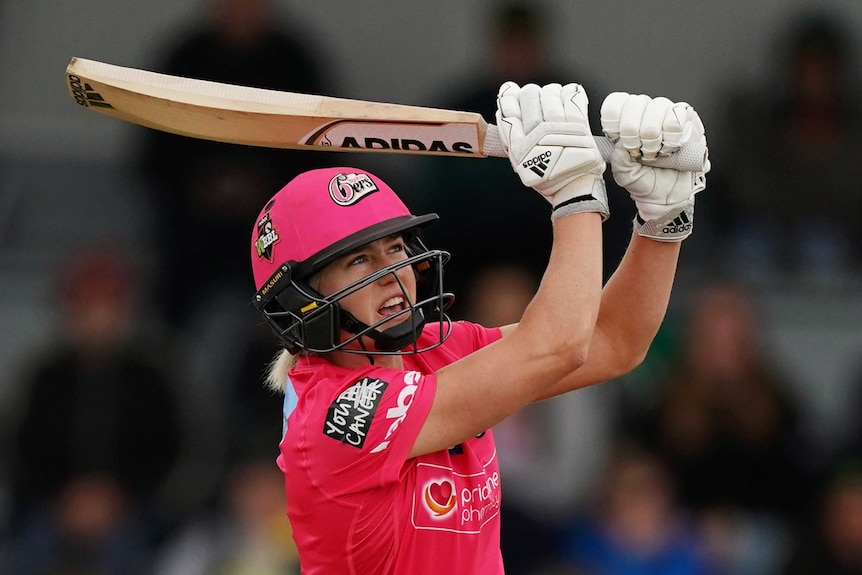 A Sydney Sixers WBBL batter wearing a helmet and holding a bat hits out to the leg side against Hobart Hurricanes.