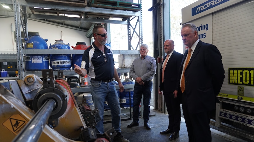 Four men in a shed looking at mining equipment