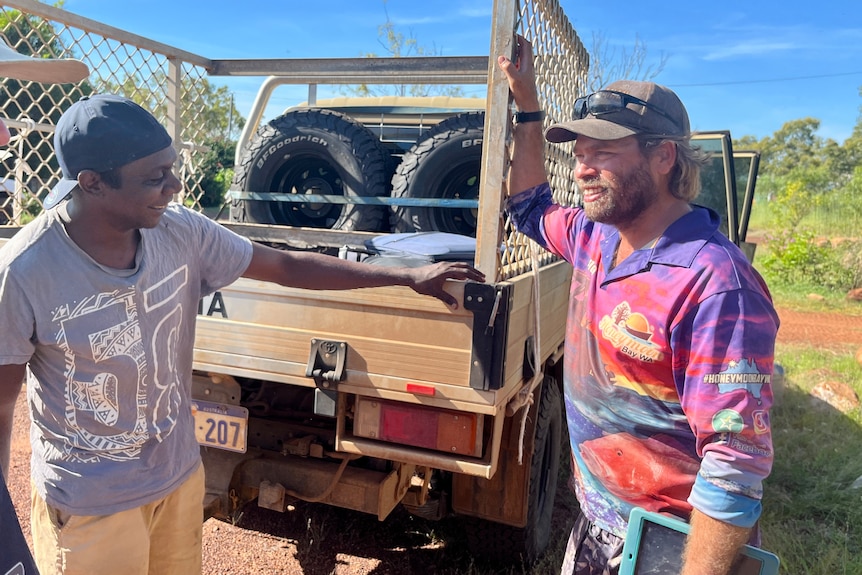 Several men stand outside chatting next to a vehicle