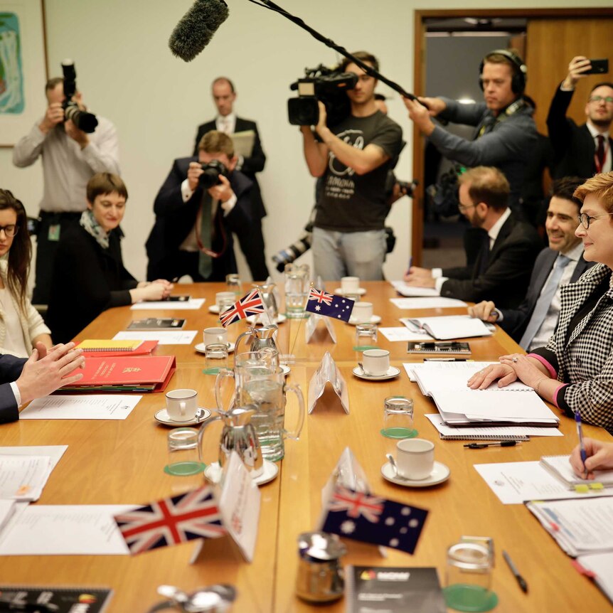 Dominic Raab and Marise Payne talk across a table surrounded by staffers and media